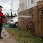 Oceanview Drive resident Dave Buffett attempts to clean graffiti off his fence using a high-pressure water hose. Police are actively investigating incidents of graffiti along Oceanview Drive.