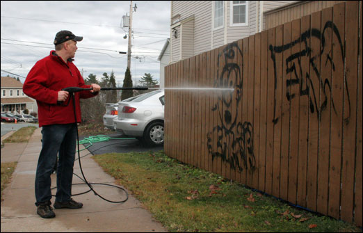 Oceanview Drive resident Dave Buffett attempts to clean graffiti off his fence using a high-pressure water hose. Police are actively investigating incidents of graffiti along Oceanview Drive.