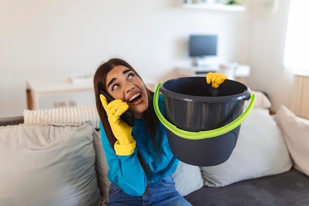 Free photo shocked woman calling plumber while collecting water leaking from ceiling using utensil