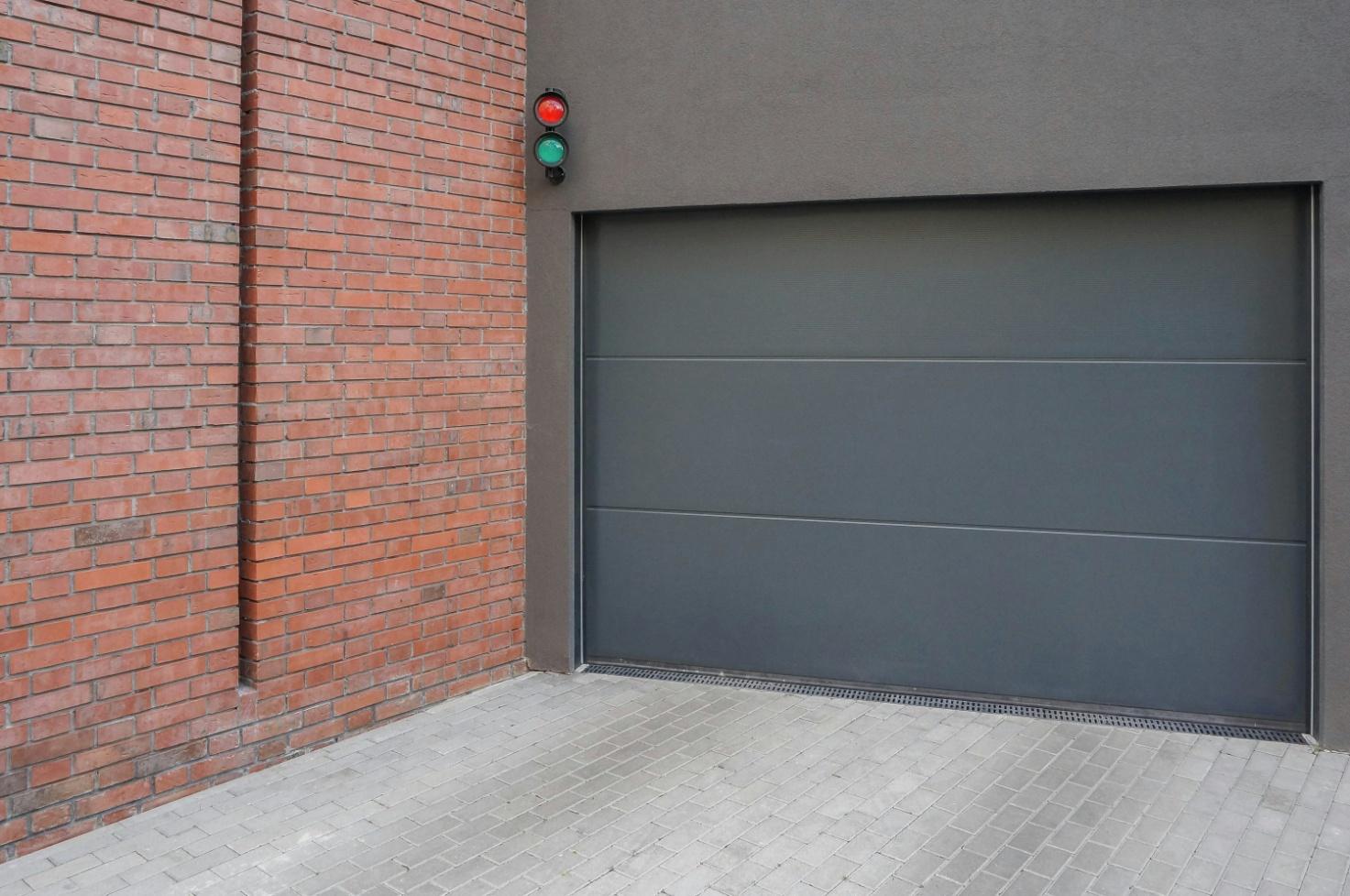 a grey garage door next to a brick wall