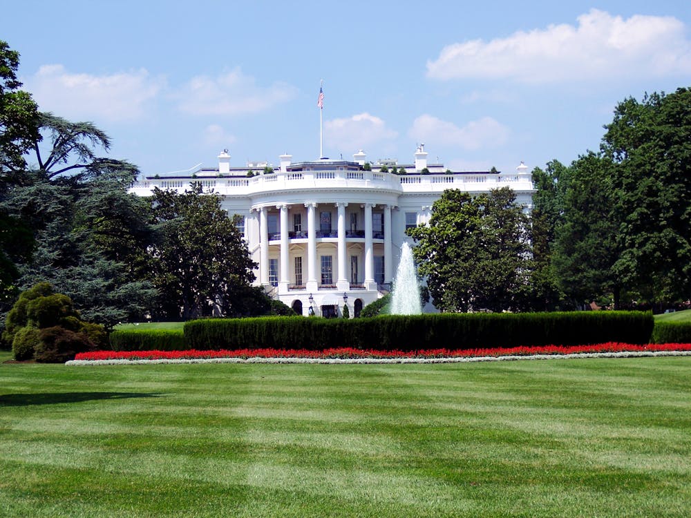 Free Iconic view of the White House with lush gardens and a central fountain on a sunny day. Stock Photo