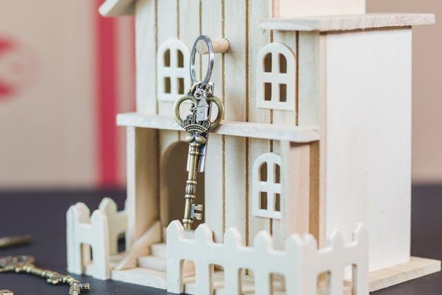 A house key hanging from a wooden model of a house.  