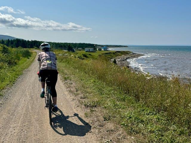 A man riding a bicycle on the trail near the sea.   