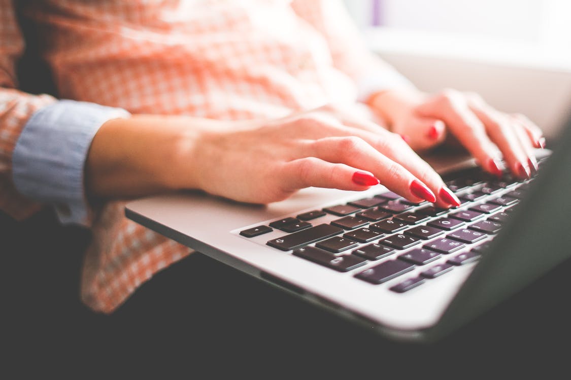 Free Close-up of a woman with red nails typing on a laptop indoors. Stock Photo